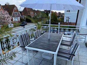 Un patio con tavolo e sedie, un ombrellone bianco e vista su case sullo sfondo.