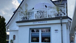 A white building with a balcony, a bench, and a sign reading 'HAUS PARKBLICK.' - Apartment 'Ferienwohnung Parkblick 2' with Private Terrace, Balcony and Wi-Fi (Lübeck Travemünde)
