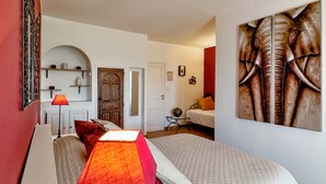 Une chambre à coucher avec un lit, une table de chevet, une lampe, une porte, une petite table avec un vase et un tableau mural.