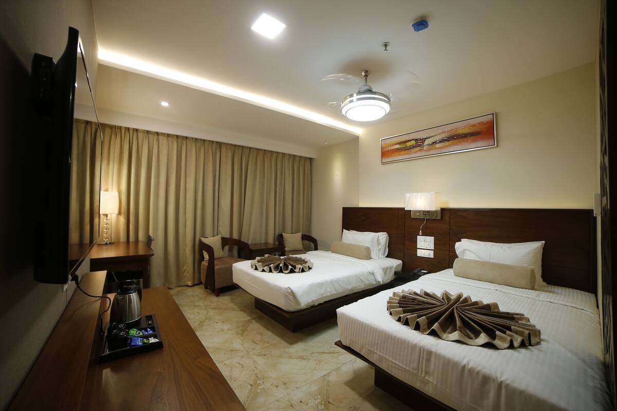 A hotel room with two beds, a desk with a coffee maker, a TV, and a ceiling fan.