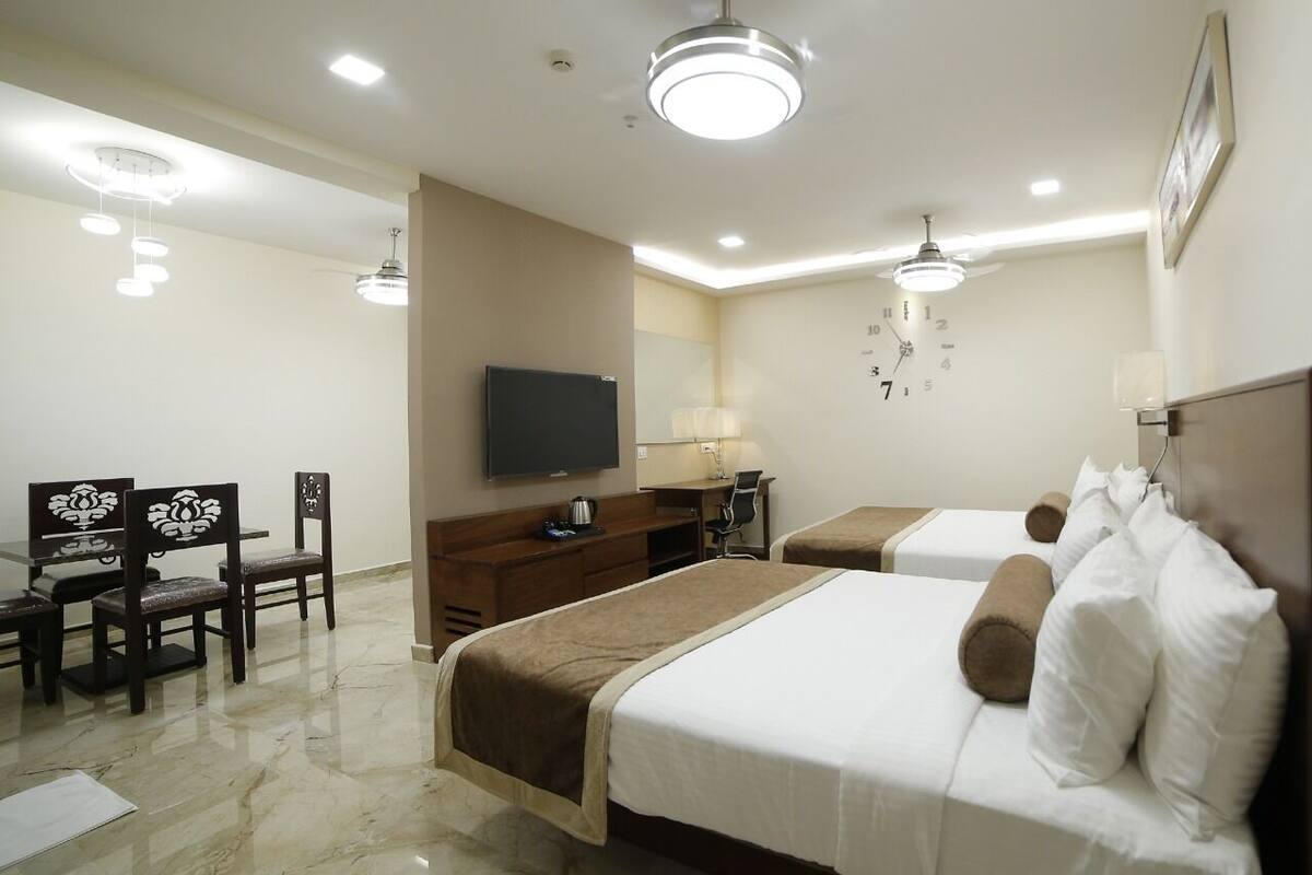 A hotel room with two beds, a desk, a chair, a TV, and a ceiling fan.