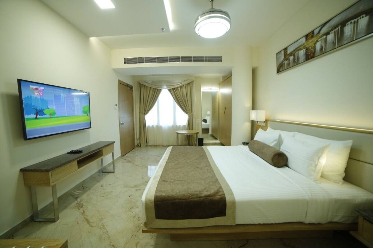 A hotel room with a large bed, a TV on the wall, a desk, and a mirror.