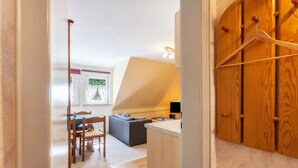 A room with a dining table, chairs, a sofa, a small kitchen area, and a wooden wardrobe with a coat hanging. - Apartment 'Wohnung 1 Birke' with Wi-Fi (Willingen (Upland))