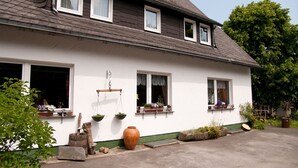 A white house with multiple windows, a large window on the ground floor, and a small porch area with potted plants. - Apartment 'Wohnung 1 Birke' with Wi-Fi (Willingen (Upland))