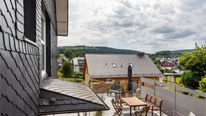 A balcony with a table and chairs, a potted plant, and a view of a house and hills. - Apartment 'Ferienhaus Doris' with Mountain View, Private Terrace and Wi-Fi (Willingen (Upland))