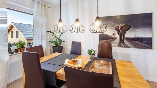 A dining area with a wooden table, black chairs, hanging pendant lights, and a large elephant painting on the wall. - Apartment 'Ferienhaus Doris' with Mountain View, Private Terrace and Wi-Fi (Willingen (Upland))