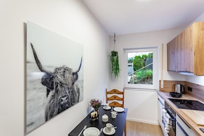 Eine moderne Küche mit Esstisch für zwei Personen, einer hängenden Pflanze und einem großen Kunstwerk an der Wand.