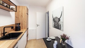 A modern kitchen with a black sink, wooden shelves, a coffee machine, and a door leading to another room. - Apartment 'Ferienhaus Doris' with Mountain View, Private Terrace and Wi-Fi (Willingen (Upland))