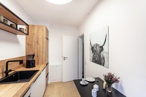 Une cuisine moderne avec un évier noir, des étagères en bois, une machine à café et une porte donnant sur une autre pièce.