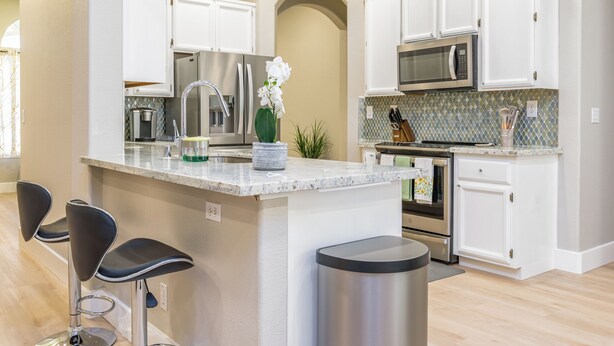 A modern kitchen with white cabinets, stainless steel appliances, and a central island with bar stools. - Charming 3Q Home w/Gourmet Backyard in Elk Grove (Elk Grove)
