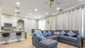 A modern living room with a grey sectional sofa, two black bar stools, a small kitchen area with a microwave, and a ceiling fan. - Charming 3Q Home w/Gourmet Backyard in Elk Grove (Elk Grove)