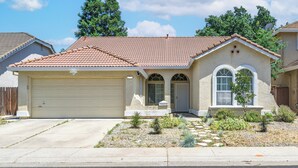 A single-story house with a red-tiled roof, a beige garage, and a small front yard with landscaping. - Charming 3Q Home w/Gourmet Backyard in Elk Grove (Elk Grove)