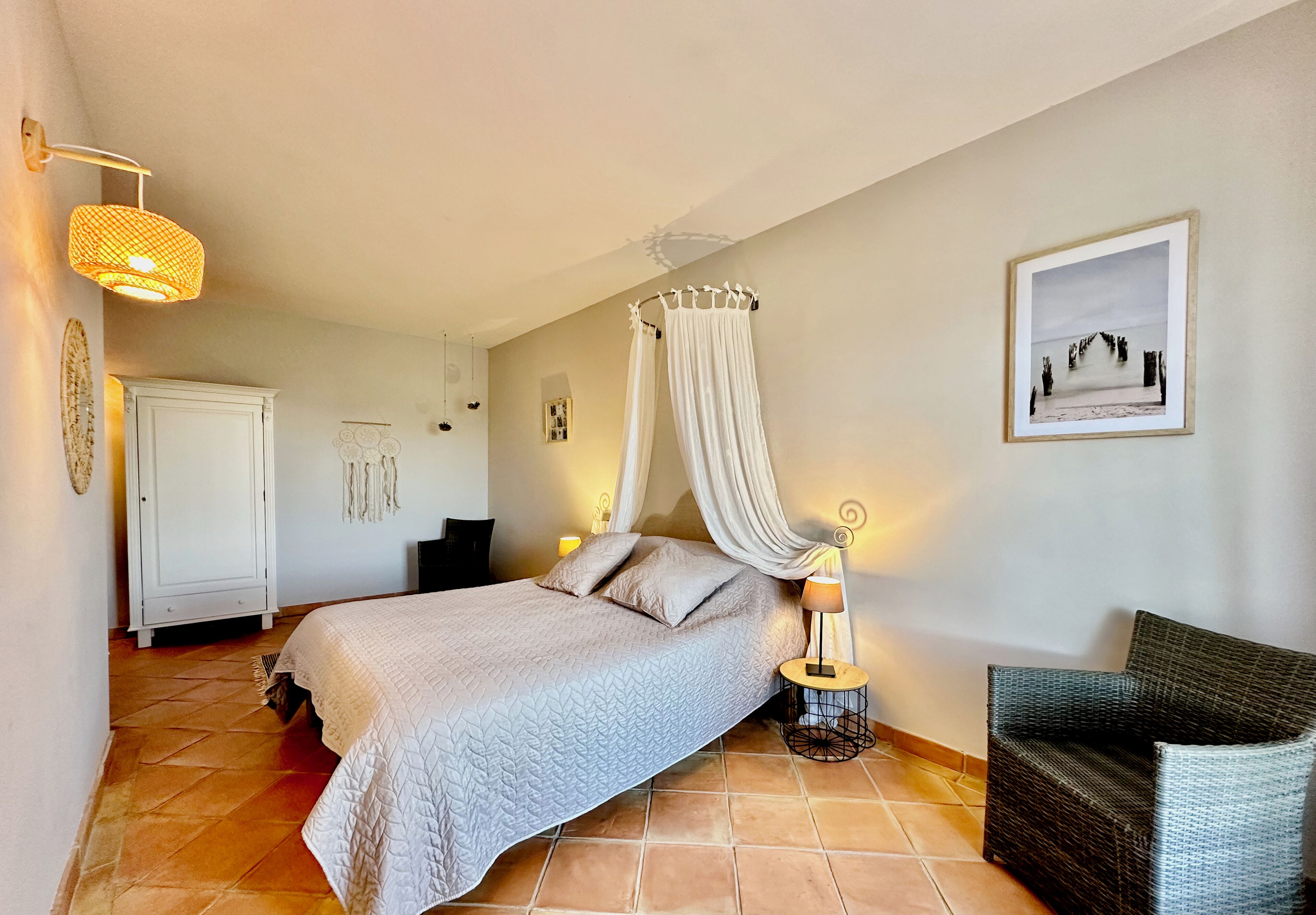 Een slaapkamer met een bed, nachtkastje, stoel, kledingkast en een aan de muur hangend schilderij.