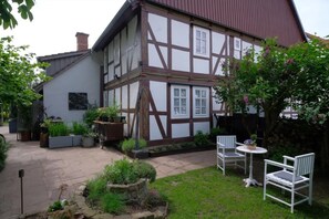 Una casa tradicional con entramado de madera y un patio jardín, con mobiliario exterior y macetas.