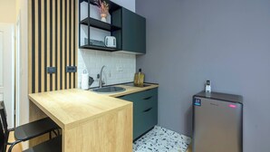 Une cuisine compacte dotée d’un plan de travail en bois, d’un évier, d’un petit réfrigérateur et d’une étagère intégrée où se trouve une bouilloire.
