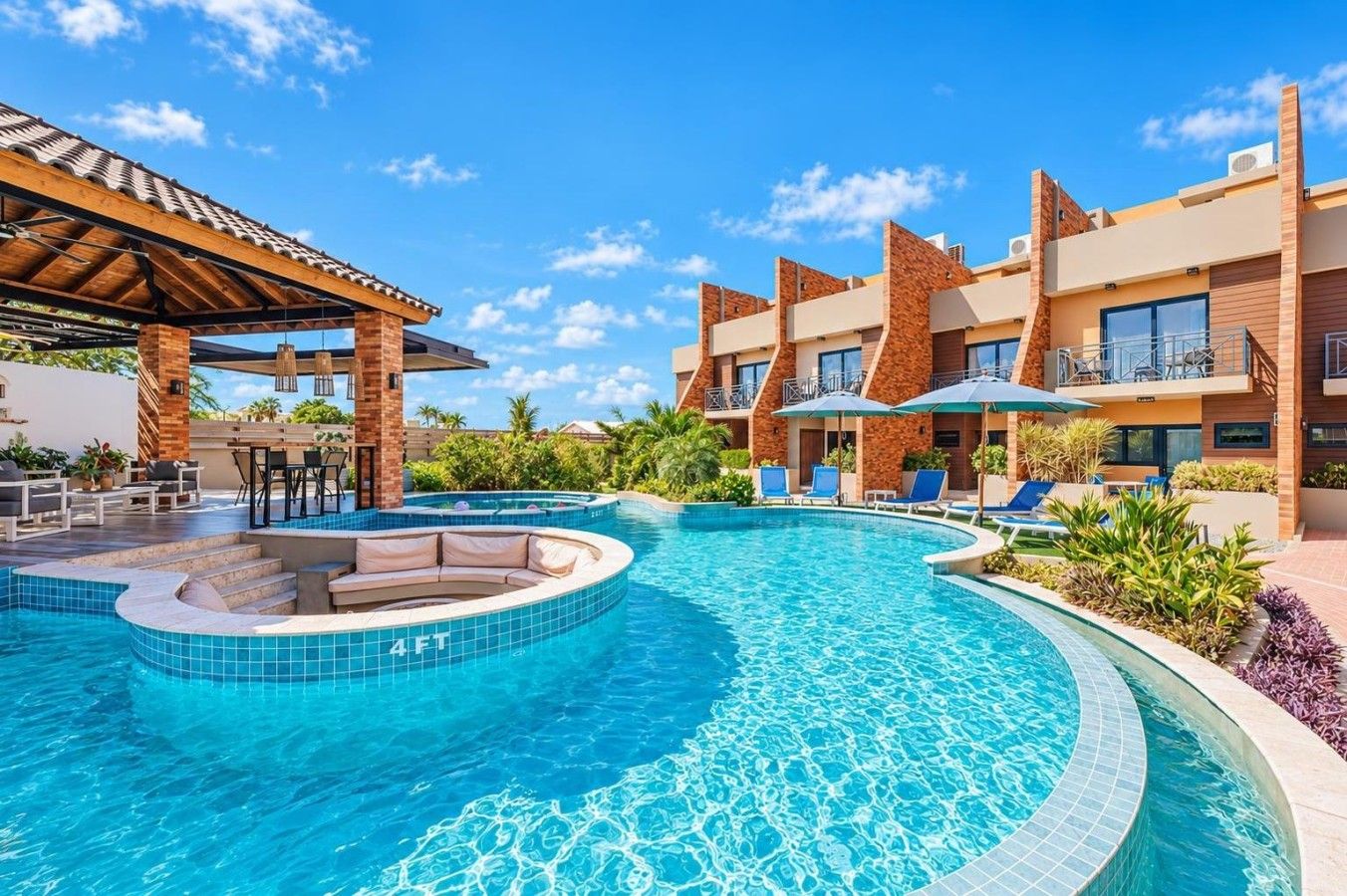 A hotel pool area with a hot tub, lounge chairs, and a covered seating area.