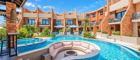 A hotel with a swimming pool, outdoor seating, and multiple balconies.