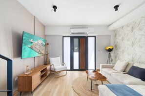 Un salon moderne avec un téléviseur à écran plat, une console en bois, un fauteuil blanc, une table basse ronde et un canapé agrémenté d’un plaid.