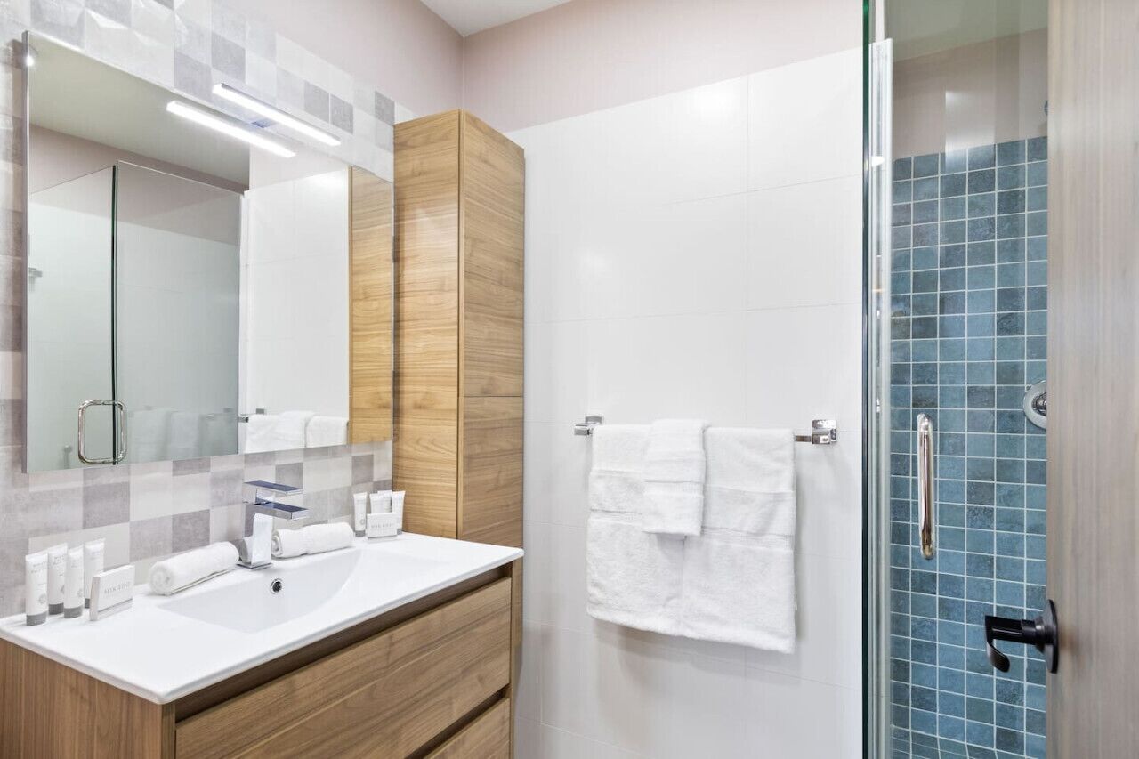 A modern bathroom with a wooden vanity, a glass shower enclosure, and a white sink.