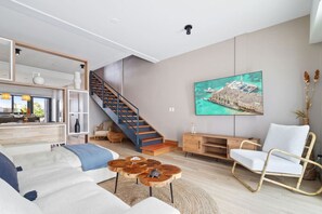 Una sala de estar moderna con una escalera, un cuadro grande y una silla blanca.