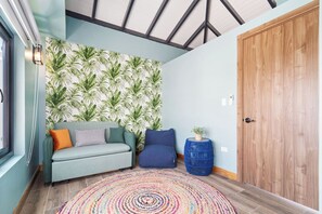 Ein Zimmer mit einer Couch, einer Wand mit Muster, einer Holztür und einem farbenfrohen Teppich.