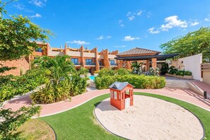 Ein Hotelinnenhof mit Pool, einem kleinen roten Spielhäuschen und einer überdachten Terrasse.