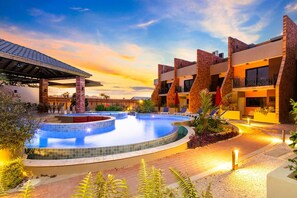 A hotel with multiple swimming pools, outdoor seating, and a sunset view.