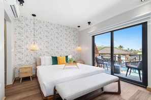 A modern bedroom with a large bed, a bench, a bedside table, and a view of a pool and outdoor area.