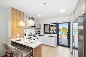 A modern kitchen with a central island, pendant lighting, and a view of an outdoor swimming pool.