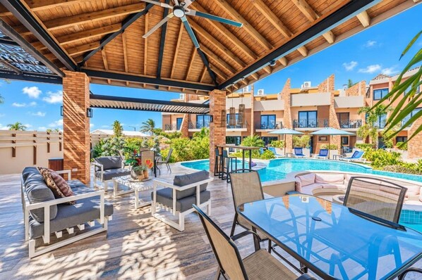 A covered outdoor area with a pool, lounge chairs, and a glass table.