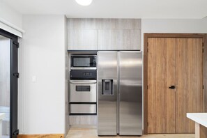 Eine kompakte Küche mit integriertem Mikrowellenherd, Backofen und Kühlschrank, einer Holztür und einer weißen Arbeitsplatte.