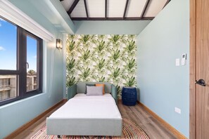 Ein Schlafzimmer mit einem Bett, einem Fenster, einer Wand mit tropischem Blattmuster und einer Tür.