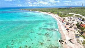 Una playa costera con aguas turquesas cristalinas, una orilla de arena y una hilera de estructuras con techo de paja a lo largo de la playa.
