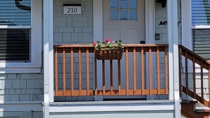 A house with a number 210 sign above the door, a wooden front porch with a railing, and a hanging flower basket. - #StayInMyDistrict Bluebird Cottage Coos Bay (Coos Bay)