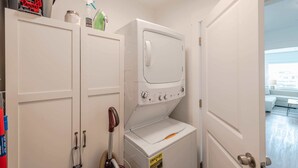 A laundry room with a front-loading washer and dryer, a mop, and cleaning supplies. - #StayInMyDistrict Bluebird Cottage Coos Bay (Coos Bay)