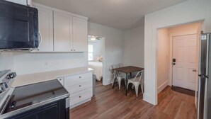 A kitchen with white cabinets, a dining table with chairs, and a refrigerator. - #StayInMyDistrict Bluebird Cottage Coos Bay (Coos Bay)