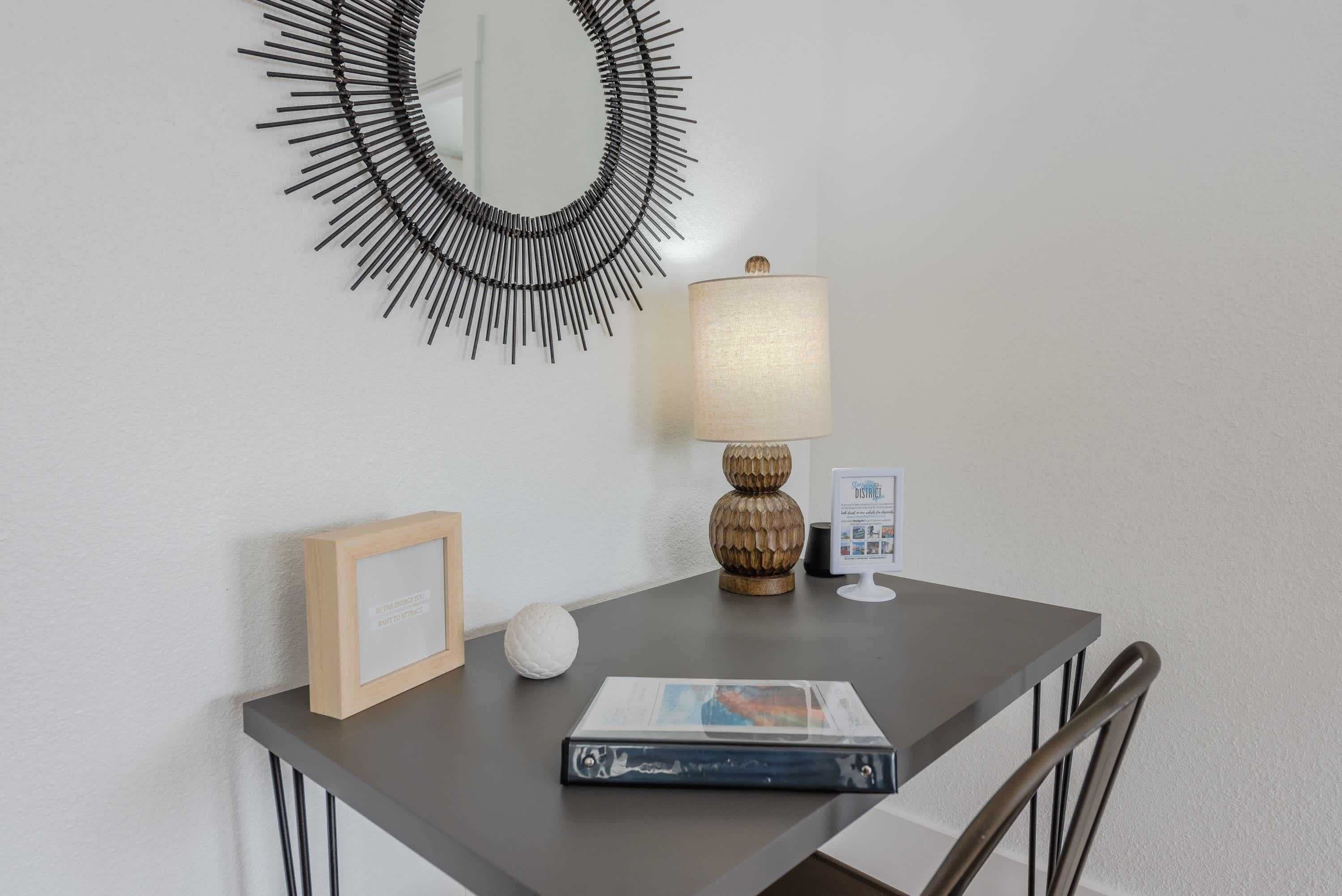 Uma pequena mesa com uma luminária, um quadro emoldurado, um objeto branco esférico e uma revista.