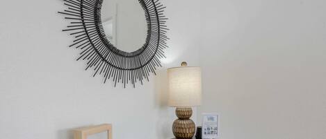 Uma pequena mesa com uma luminária, um quadro emoldurado, um objeto branco esférico e uma revista.