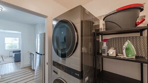 A compact laundry room with a front-loading washing machine, a dryer, and a shelf with cleaning supplies.