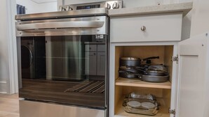 A modern kitchen with a built-in oven and a storage cabinet containing cookware and dishes.