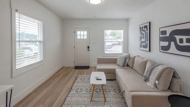 Un salon moderne avec un canapé beige, un tapis à motifs et des œuvres d’art abstraites accrochées au mur.