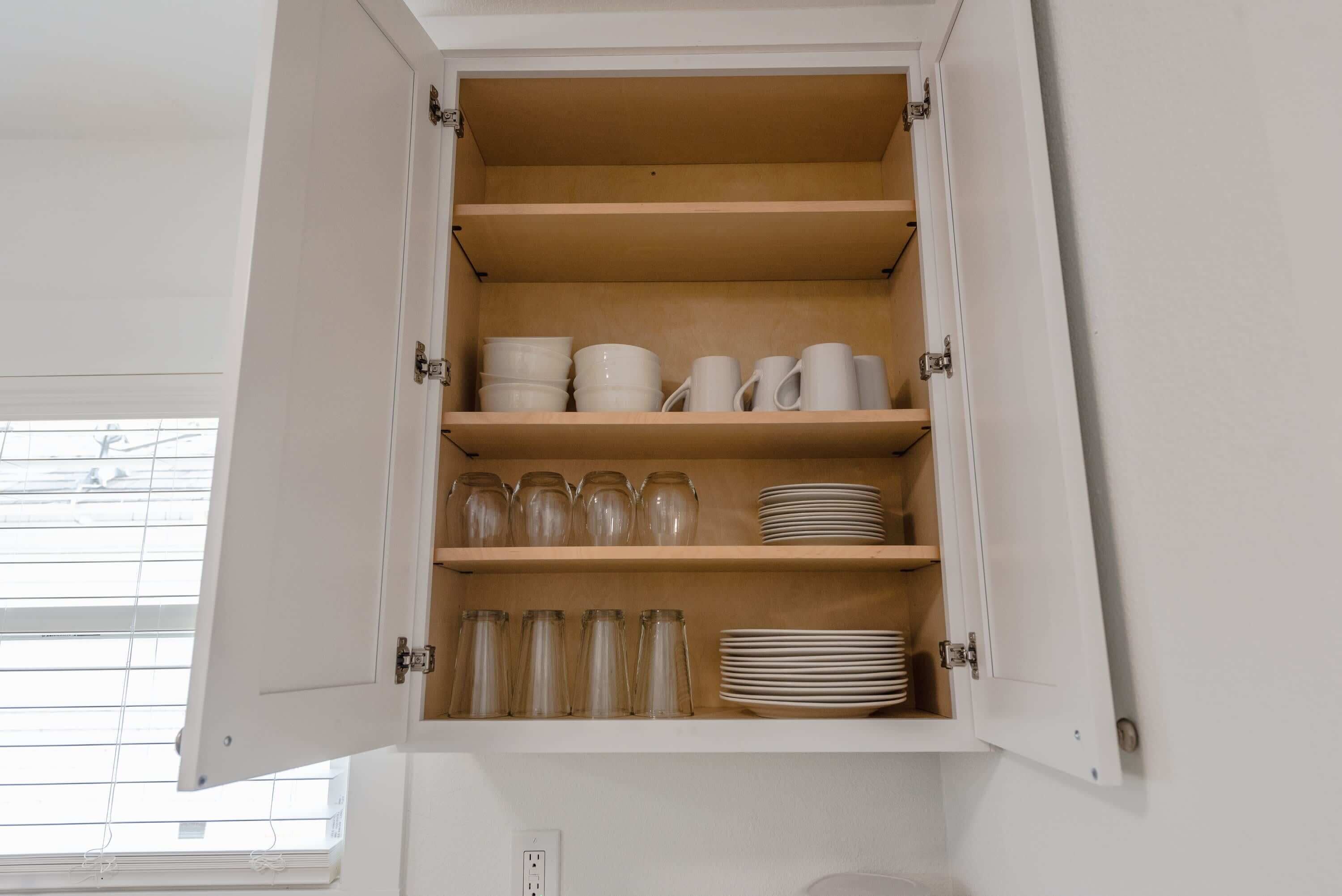 Un meuble de cuisine doté de plusieurs étagères contenant des bocaux en verre, des assiettes et des tasses.