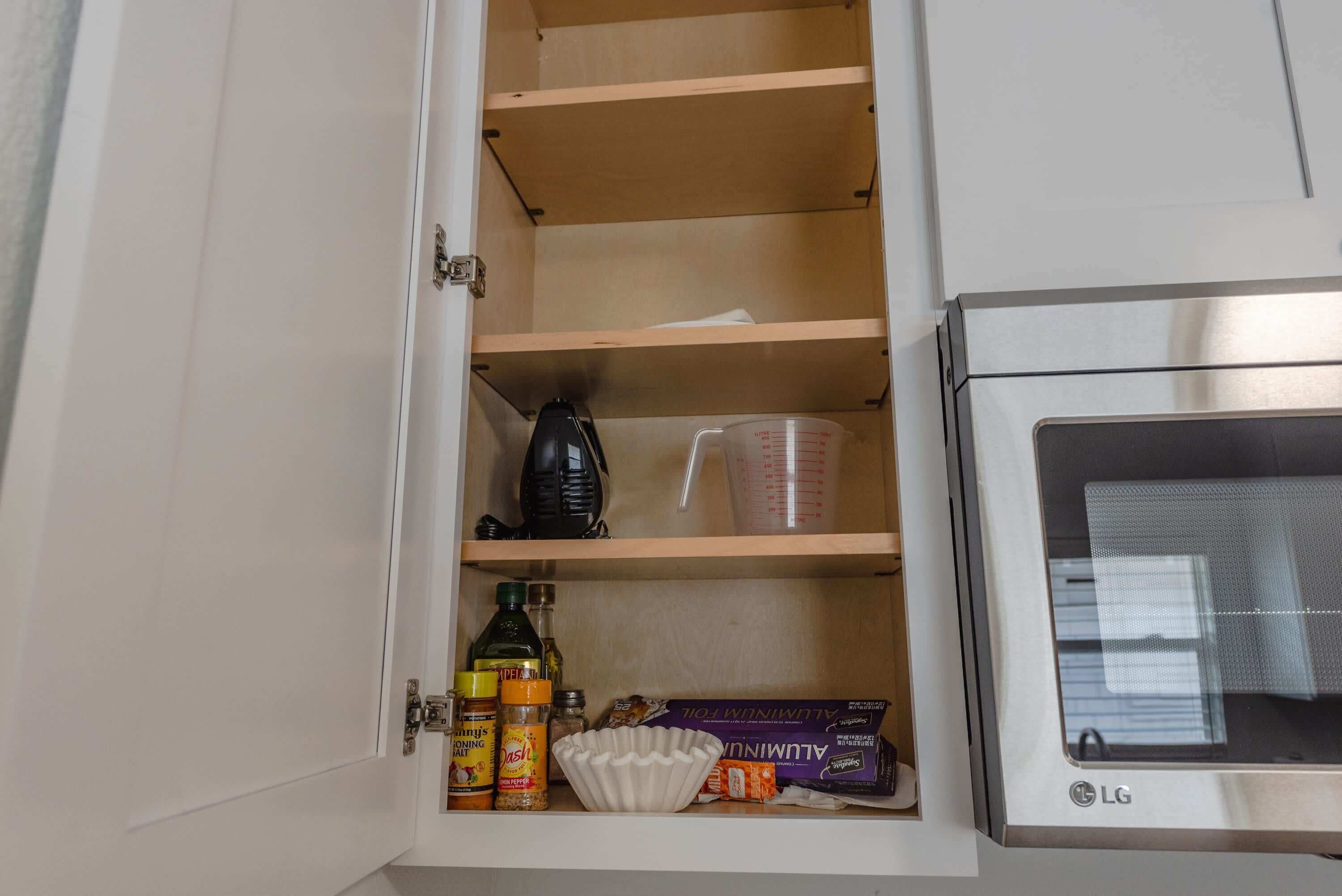 A kitchen cabinet with shelves, a measuring cup, a colander, and some packaged food items.