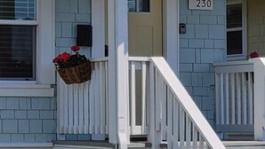 Un bâtiment à deux étages avec un porche blanc et un petit panier de fleurs.