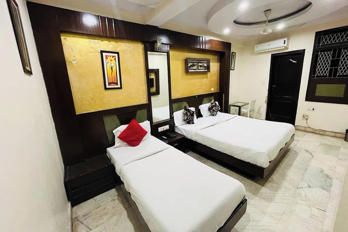 A hotel room with two single beds, a small table, a chair, and a ceiling fan.