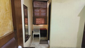 A narrow hallway with a wooden door, a white plastic chair, and a small table with a book and a green object. - Hotel Spot Inn Paharganj Near New Delhi Railway Station (New Delhi)