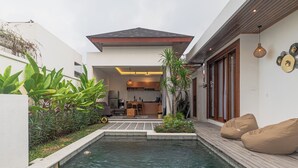A modern house with a swimming pool, a wooden deck, and a kitchen visible through an open door. - Cypress Villa (Ungasan)