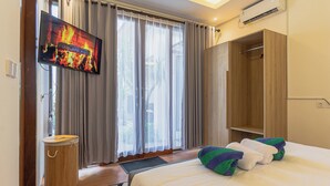 A hotel room with a bed, a TV mounted on the wall, a wardrobe, and a window with curtains. - Cypress Villa (Ungasan)