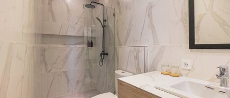 Un baño moderno con ducha de vidrio, inodoro blanco y tocador de madera con lavamanos.