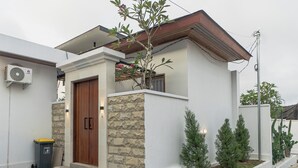 A modern house with a stone facade, a wooden door, and a small garden with potted plants. - Cypress Villa (Ungasan)